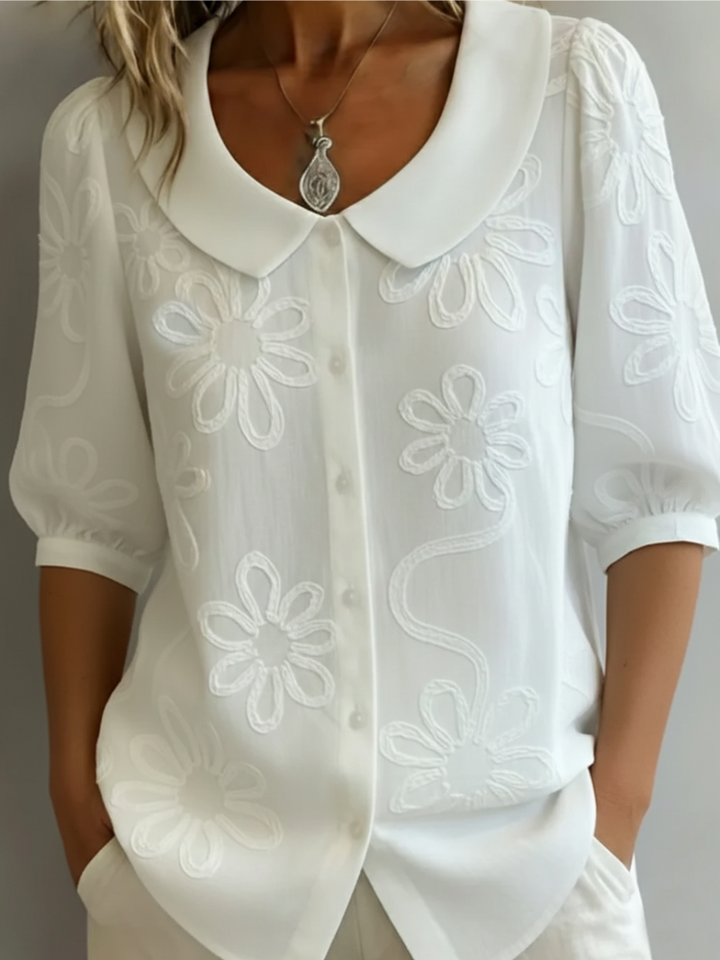 Chic women's summer blouse featuring delicate floral embroidery and short sleeves. A stylish and comfortable top for everyday wear.