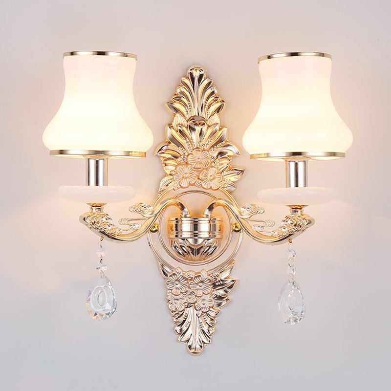 Elegant Victorian wall lamp with a detailed gold finish, white shade, & hanging crystal decorative pieces.