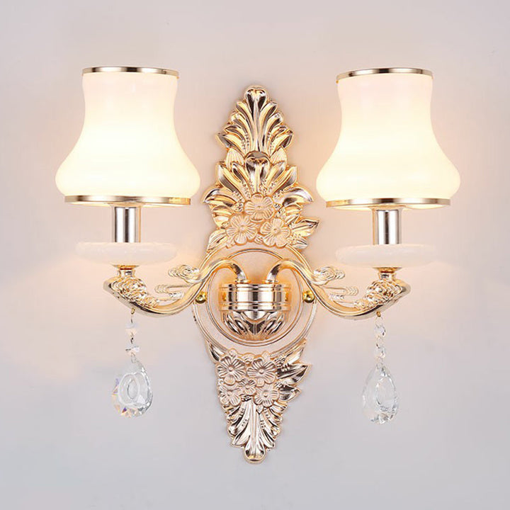 Elegant Victorian wall lamp with a detailed gold finish, white shade, & hanging crystal decorative pieces.