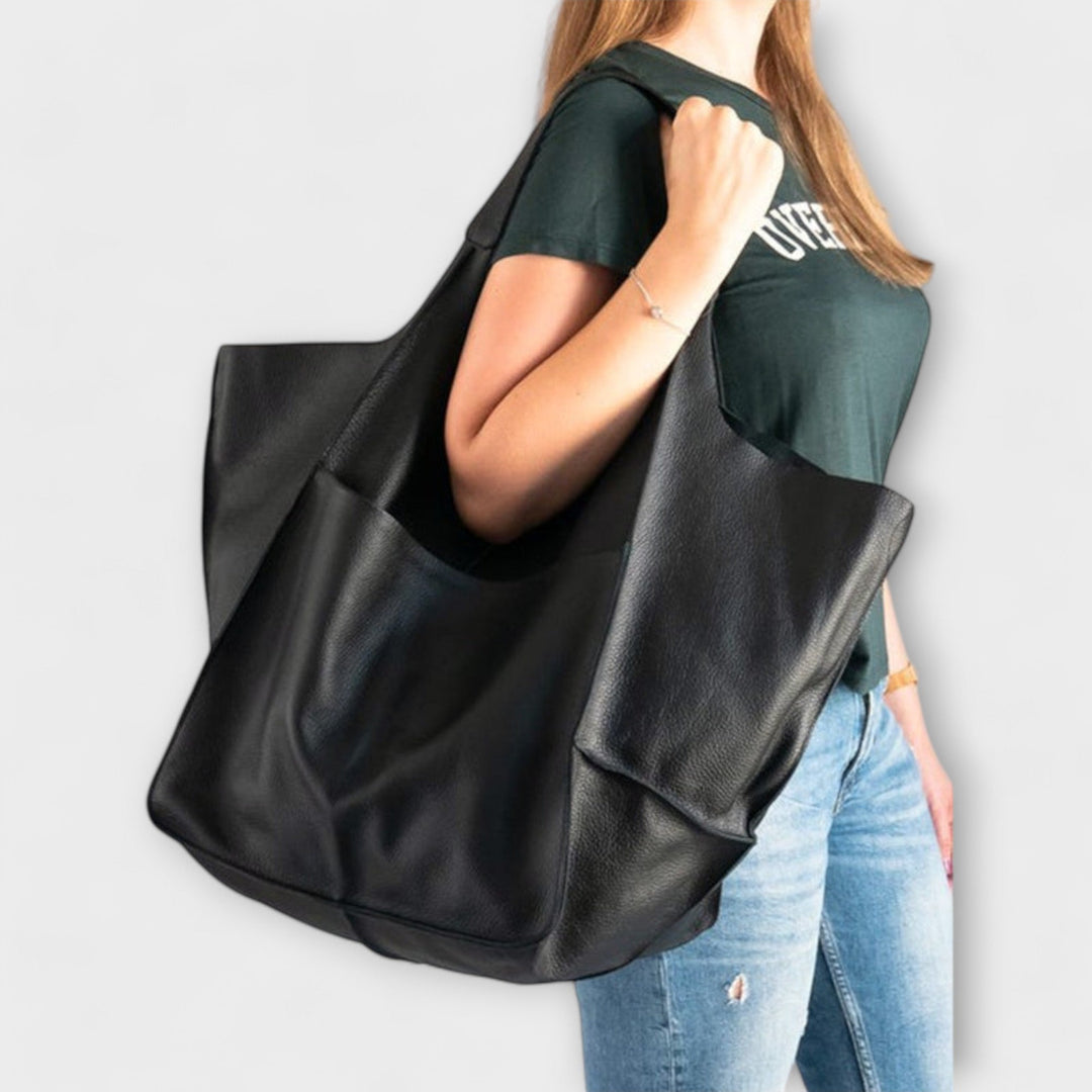 A woman packing her essentials into an oversized leather carryall travel bag.