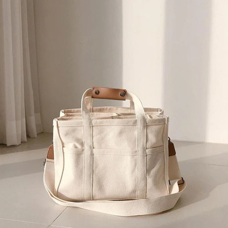 Stylish women's canvas tote bag with multiple pockets, can be worn as a shoulder or crossbody bag.