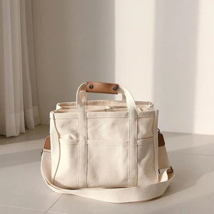 Stylish women's canvas tote bag with multiple pockets, can be worn as a shoulder or crossbody bag.