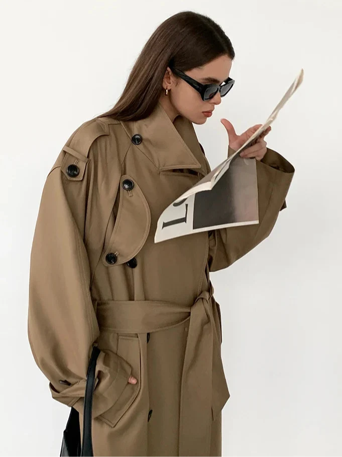 Chic women's oversized long trench coat in gray, styled with a detachable belt to cinch the waist for a modern look.