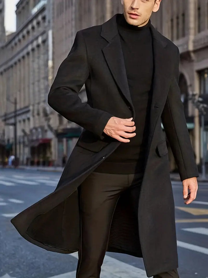 Man wearing a sleek slim fit long trench coat. This notched lapel men's outerwear is perfect for winter style.