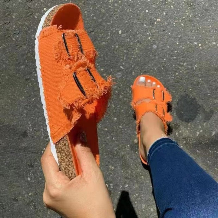 Fashionable women's distressed flat sandals in denim style. Casual open-toe footwear for summer comfort.