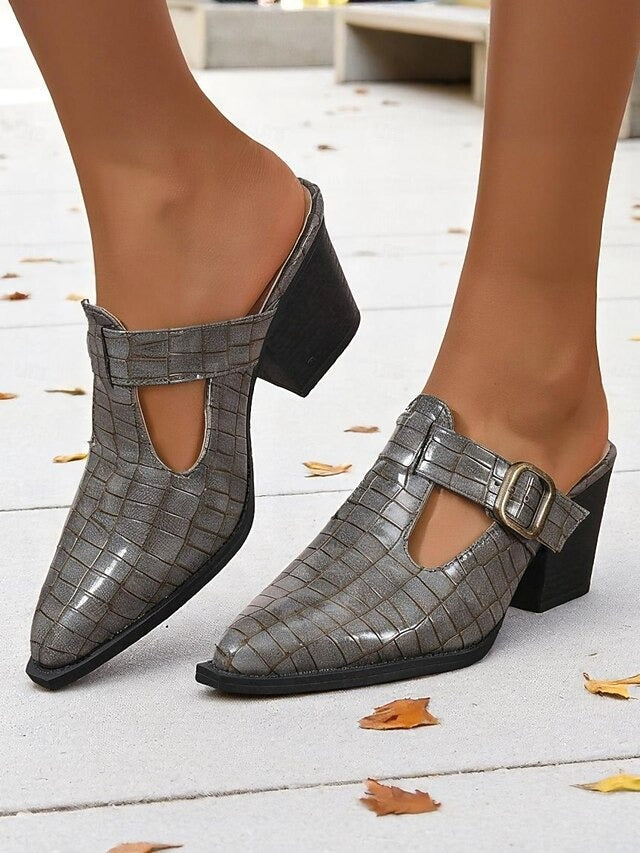 Fashionable women's mules featuring a block heel, unique cut-out design, and stylish buckle detail. Slip-on comfort.