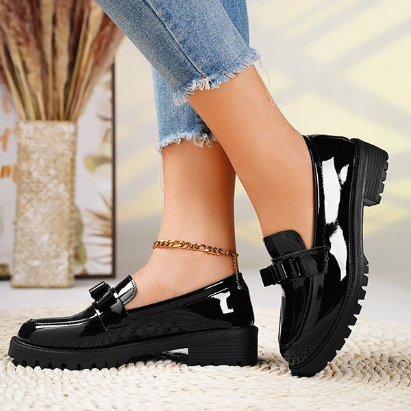 High-shine black platform slip-on loafers for women, featuring a sophisticated bow and lug sole.