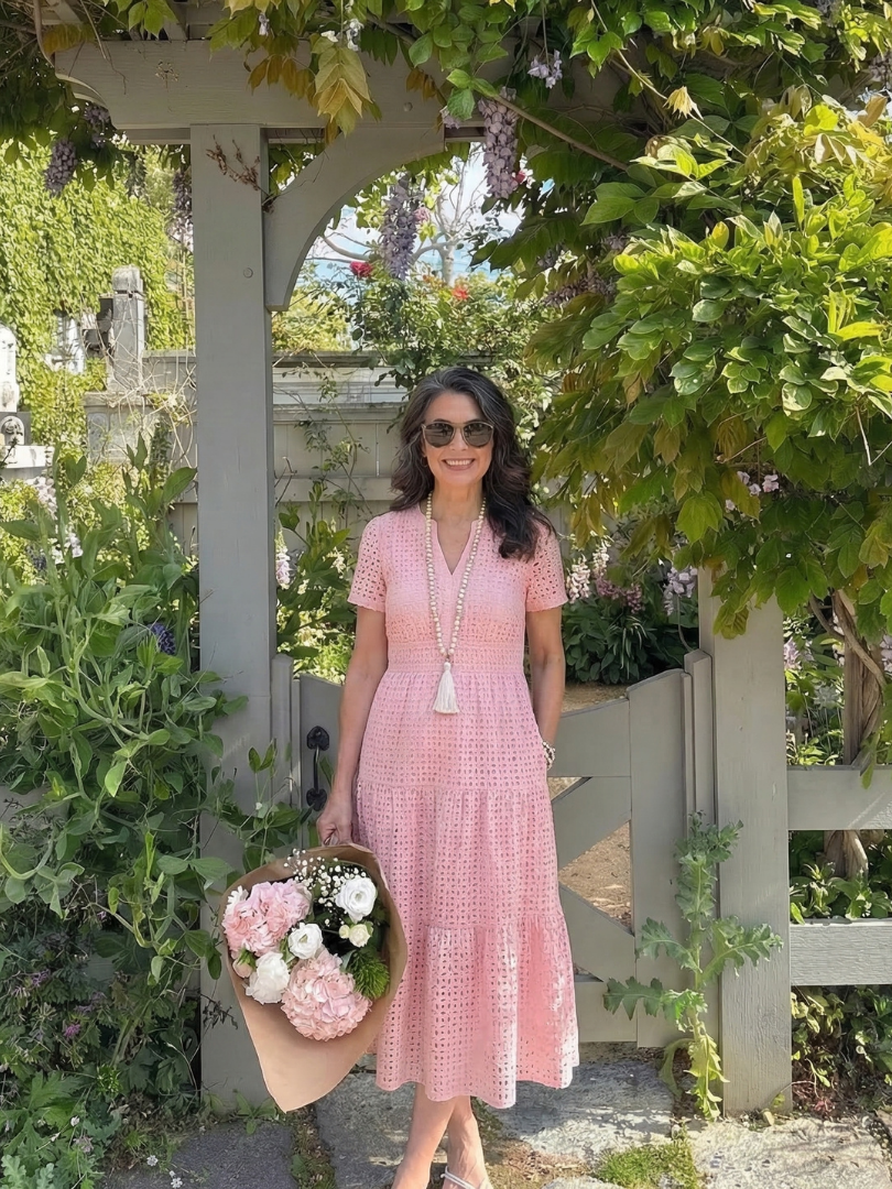 Full-length view of a feminine white eyelet midi dress featuring a stylish tiered skirt and short sleeves.