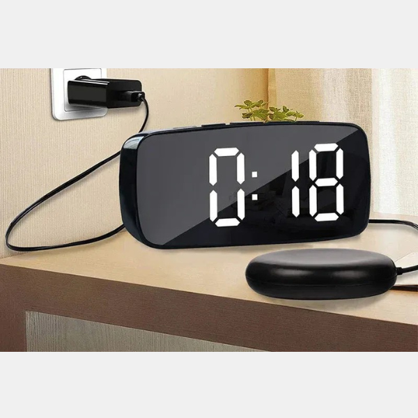 Close-up of a black vibrating alarm clock's digital display with time. Bed shaker included for a powerful wake-up.