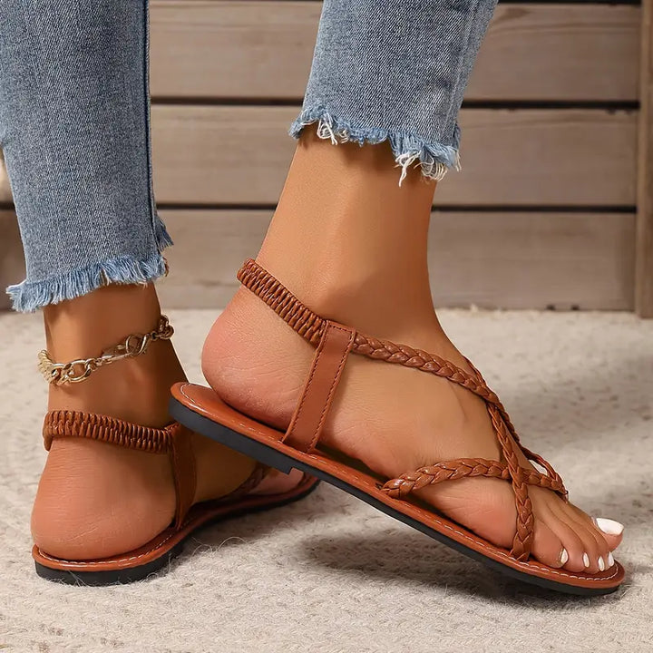 Women's feet wearing elegant braided flat sandals with toe ring, showcasing casual summer style.