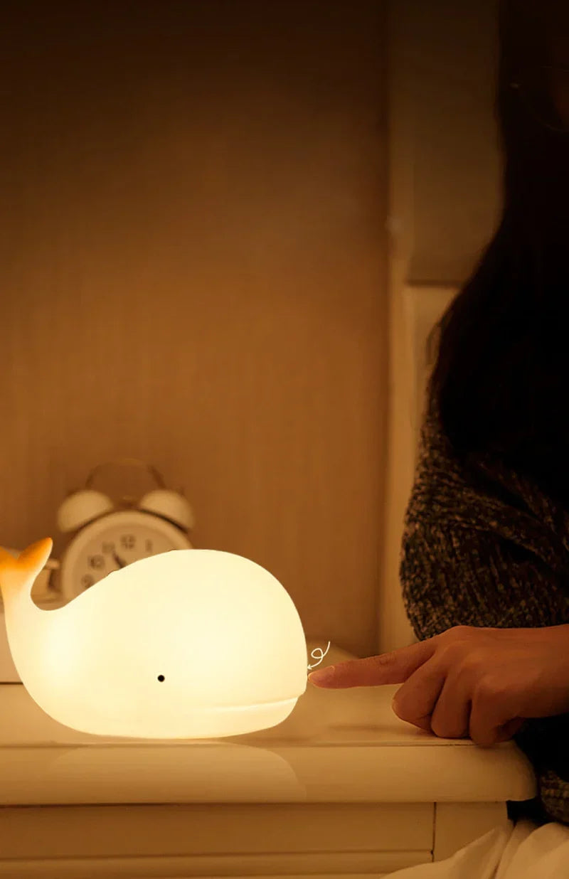 Adorable white whale bedside lamp with touch control. Emits calming, color-changing LED light for kids' rooms.