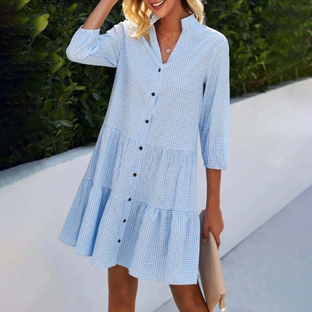 Woman wears relaxed blue gingham tiered button-down midi dress, perfect for casual summer outings or brunch. Comfortable preppy style.