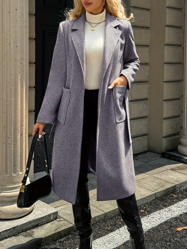 Women's elegant belted trench coat in an office setting. Sophisticated tailored outerwear for work.