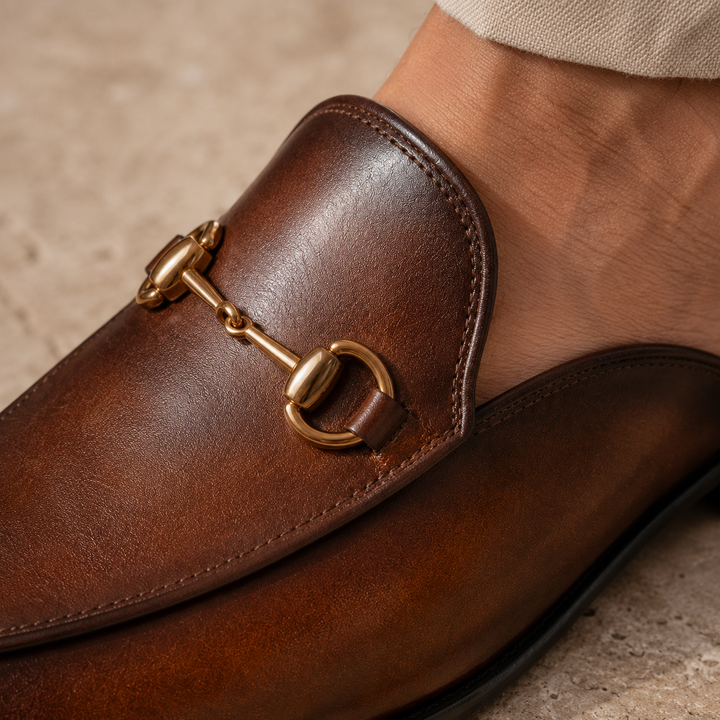 Elegant men's slip-on mules with distinctive horsebit detail, perfect for sophisticated casual wear.