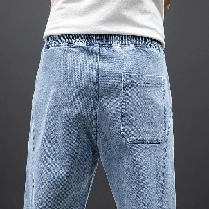 Modern men's blue stretch denim joggers with elastic waist and tapered leg for versatile, comfortable casual style.