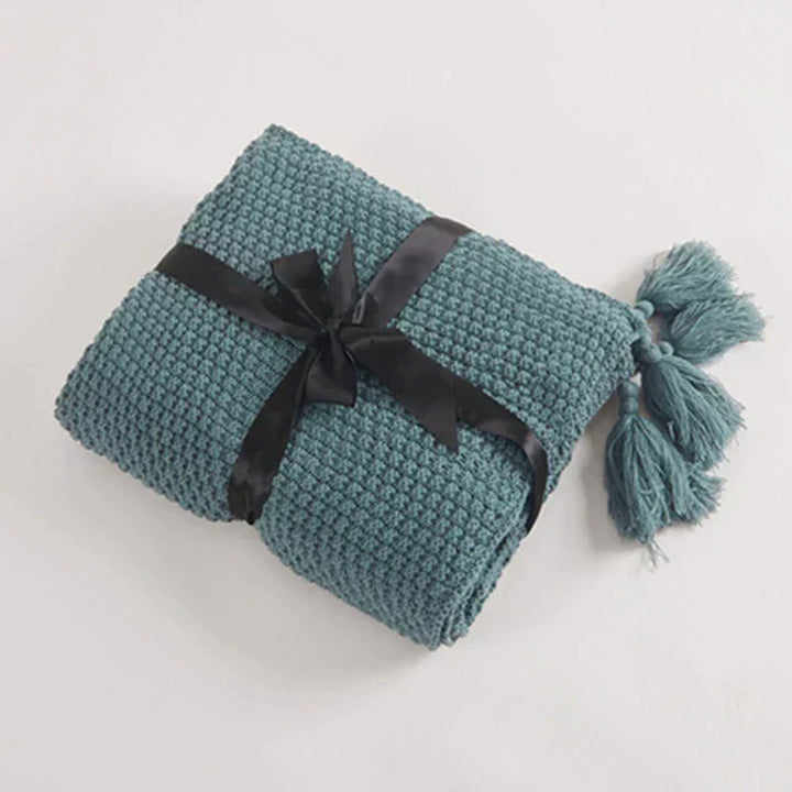 Elegant knitted wool blanket, decorative tassels, ideal for a refined bedroom aesthetic.