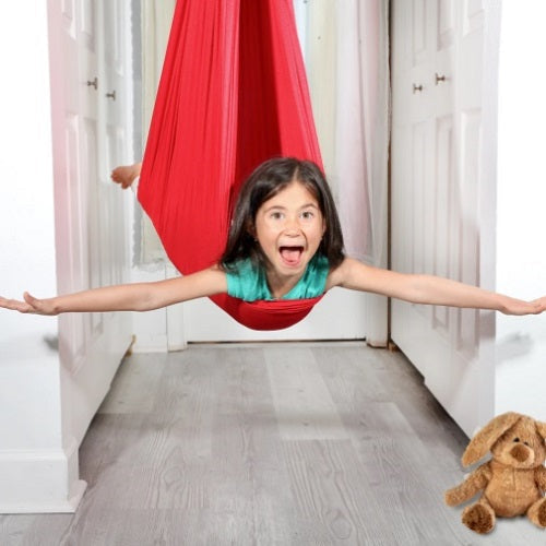 Happy child in a calming sensory swing, enjoying deep pressure for focus & sensory development in a playroom.