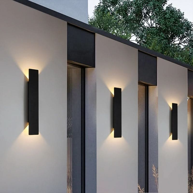 Sleek black modern LED outdoor wall light sconce illuminating a patio entrance. Energy-efficient exterior lighting.