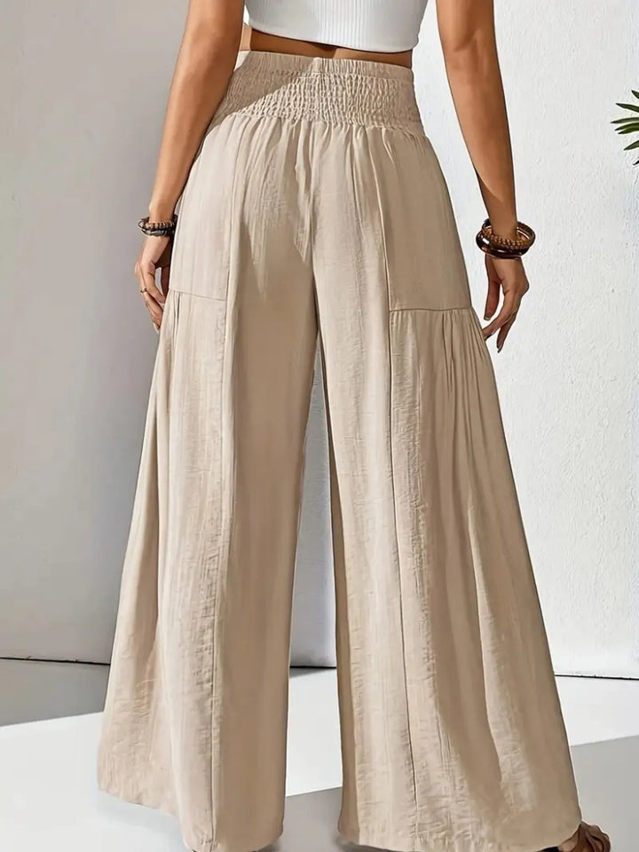 Model wearing casual wear: women's flowy wide leg pants with a smocked waist.
