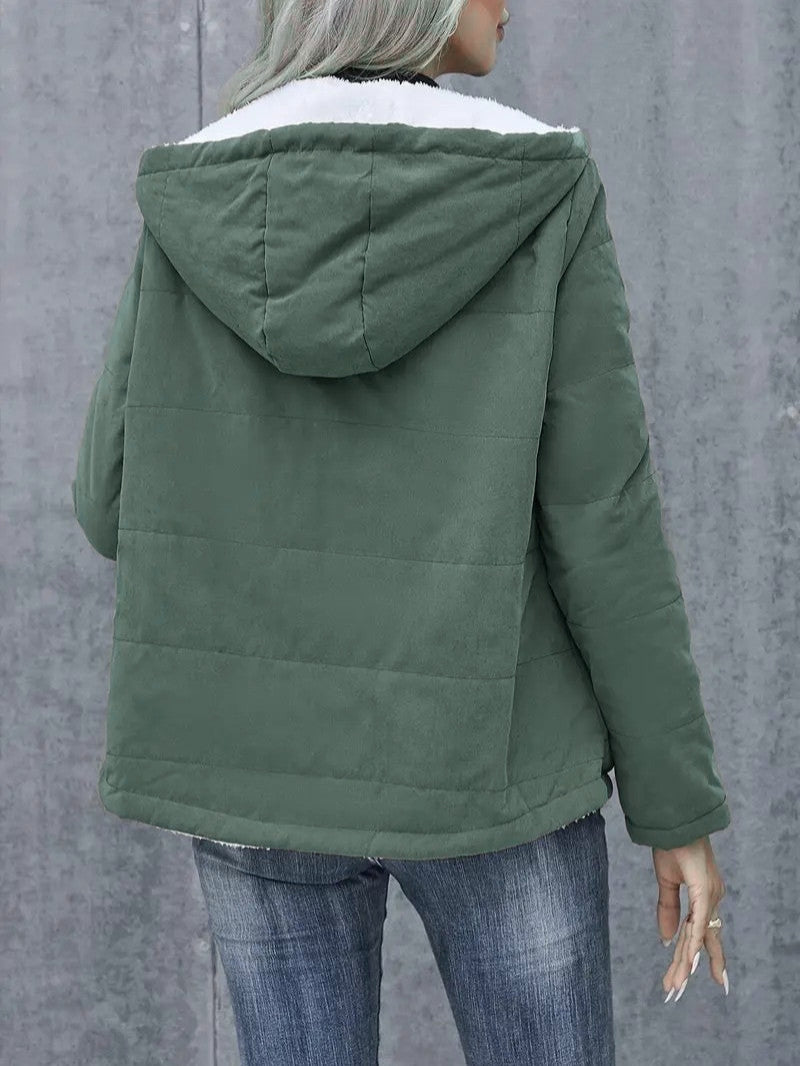 A full-length shot of a woman in a hooded, zip-up winter jacket.