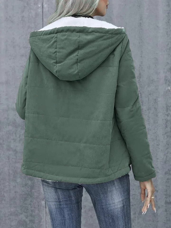 A full-length shot of a woman in a hooded, zip-up winter jacket.
