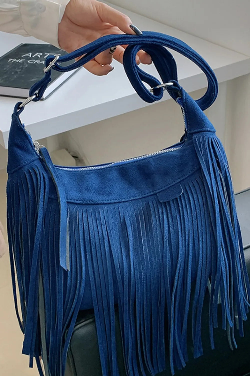 Durable suede crossbody bag with secure closure and fringe accent.