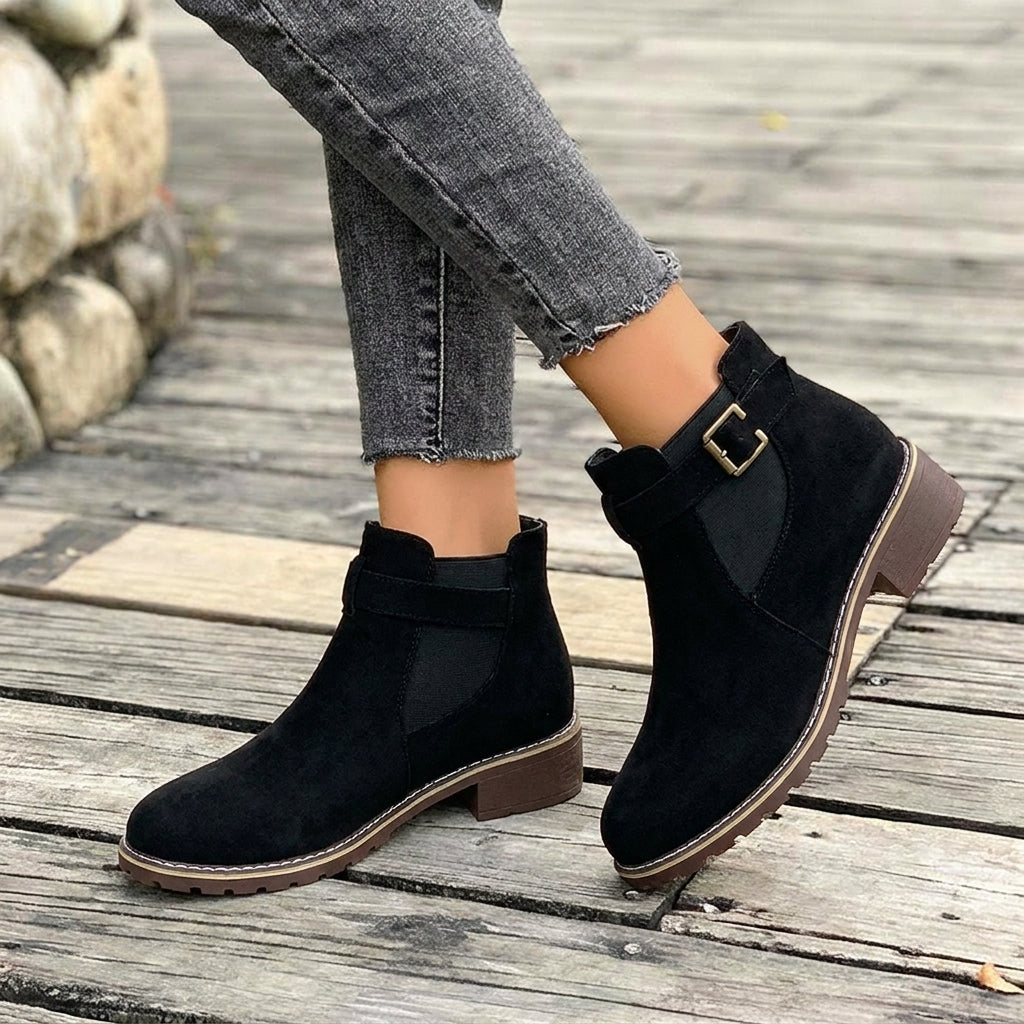 Close-up of a women's black Chelsea boot with a chic buckle strap detail, block heel, and elegant pointed toe.